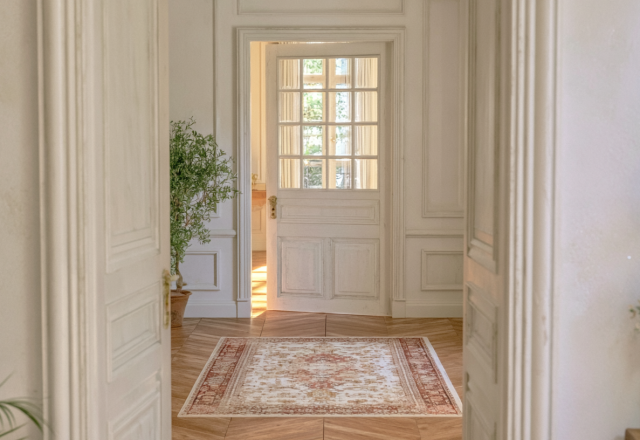 Bright interior hallway featuring chevron wood flooring, a vintage runner rug, and classic white paneled doors.
