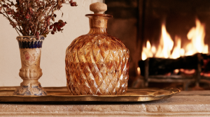 Amber glass decanter and vintage vase styled on a brass tray atop a stone mantelpiece with a fireplace