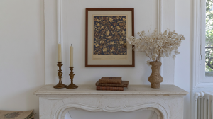 A minimalist fireplace mantel decorated with vintage botanical art, brass candlesticks, and dried florals.