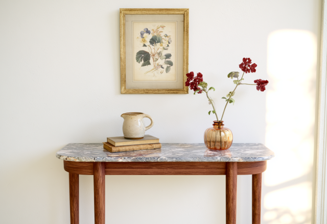 Console table styling with marble top, framed botanical art, and amber glass vase in a bright entryway.