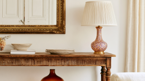 Vintage gold mirror and speckled ceramic lamp on a rustic wooden console table in a living room.