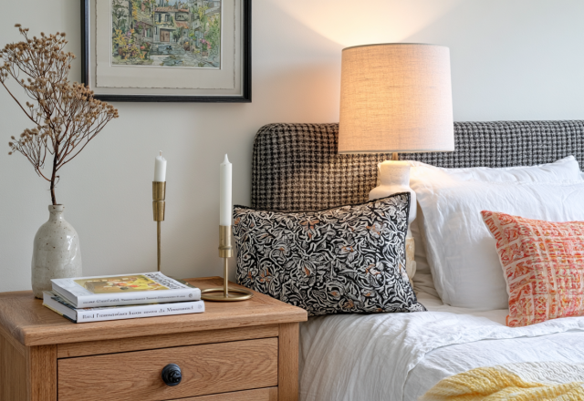 Cozy nightstand styling featuring a wooden bedside table, ceramic lamp, candles, and framed art in a neutral master bedroom.