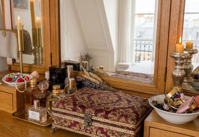 Vintage vanity table organization featuring perfume bottles, brass candleholders, and a velvet jewelry box.