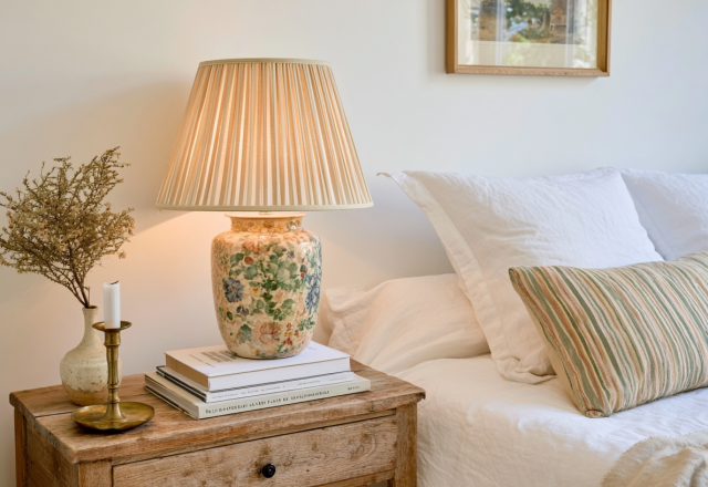 Cozy bedroom styling featuring a rustic wooden nightstand with a vintage floral lamp and books.