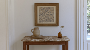 Console table styling featuring a marble top, vintage art, ceramic jug, and a bud vase in a minimalist hallway setup.