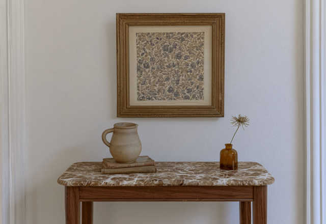 Console table styling featuring a marble top, vintage art, ceramic jug, and a bud vase in a minimalist hallway setup.