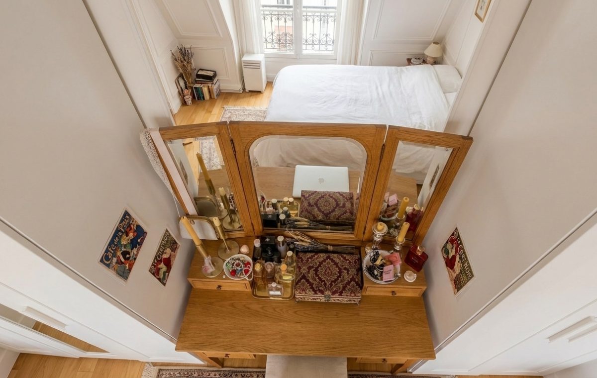 Overhead view of a wooden dressing table organization setup with triple mirrors in a small bedroom
