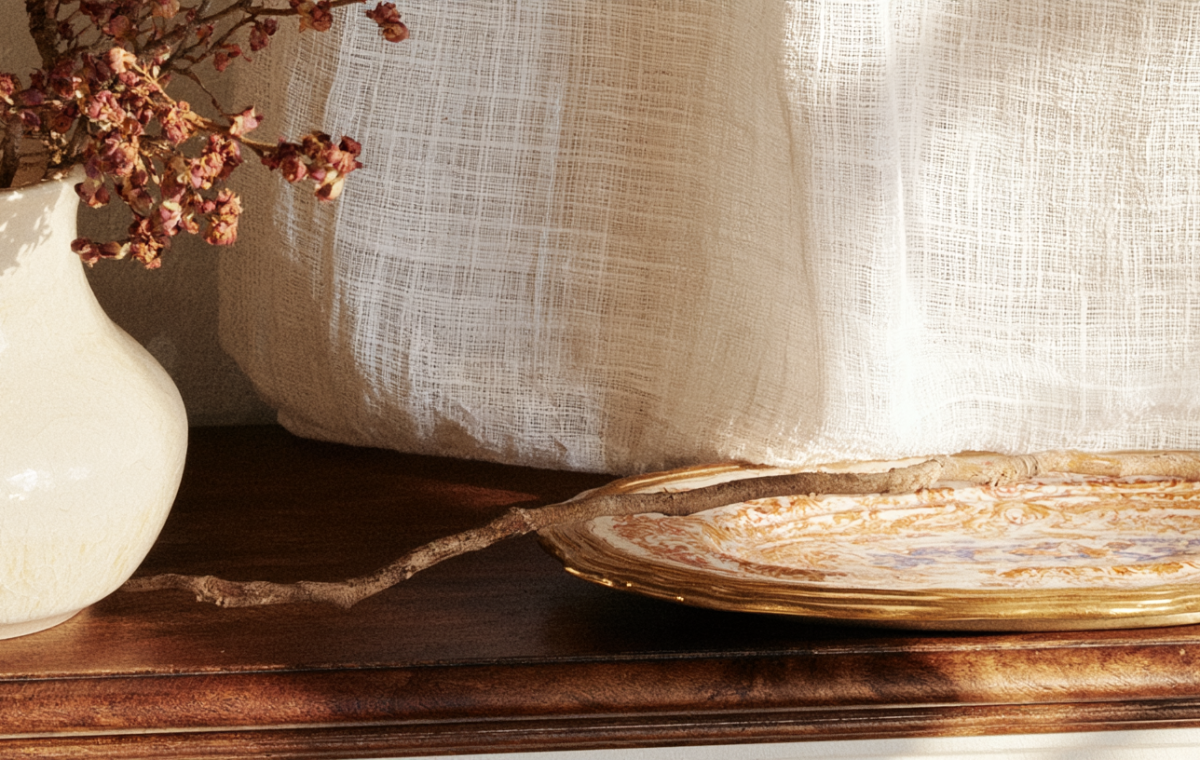 Rustic mantle decor featuring a vintage ceramic vase with dried stems and a decorative tray on a wooden console.