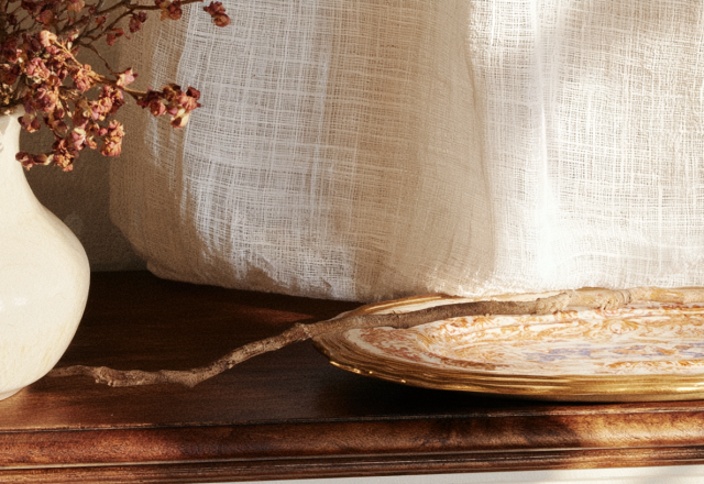 Rustic mantle decor featuring a vintage ceramic vase with dried stems and a decorative tray on a wooden console.