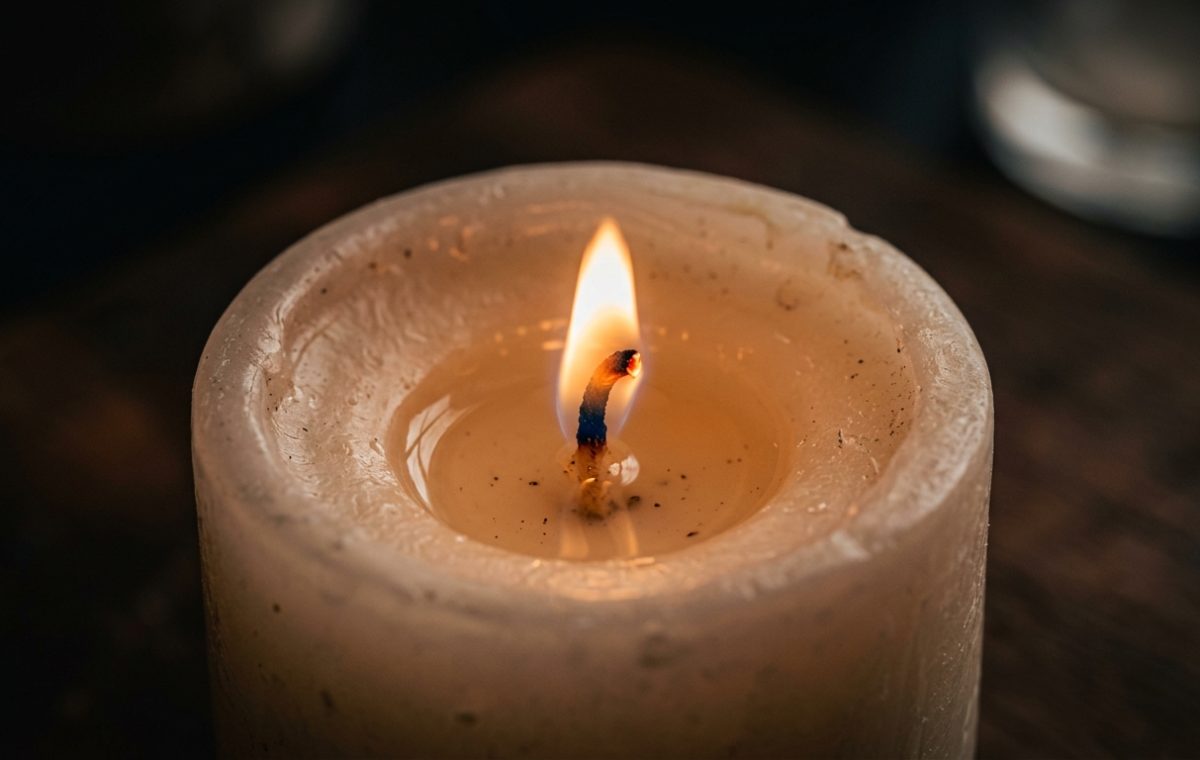 Close-up of a burning candle with a glowing flame and melted wax pool on a dark surface.