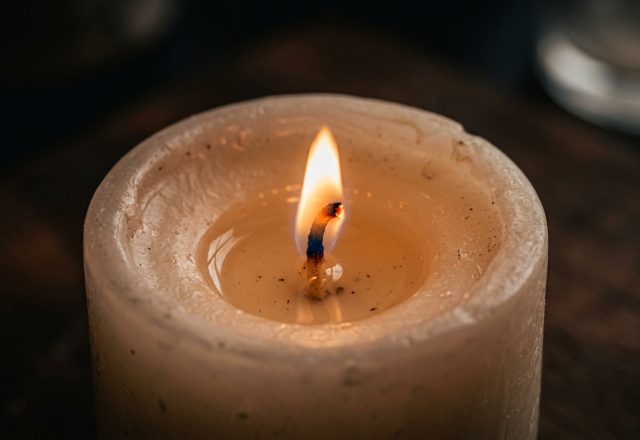 Close-up of a burning candle with a glowing flame and melted wax pool on a dark surface.