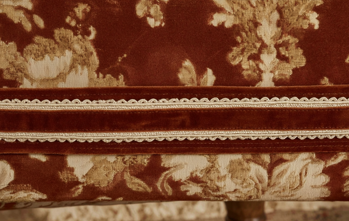 Close-up view of intricate upholstery trim details featuring crimson fabric and gold braided gimp.
