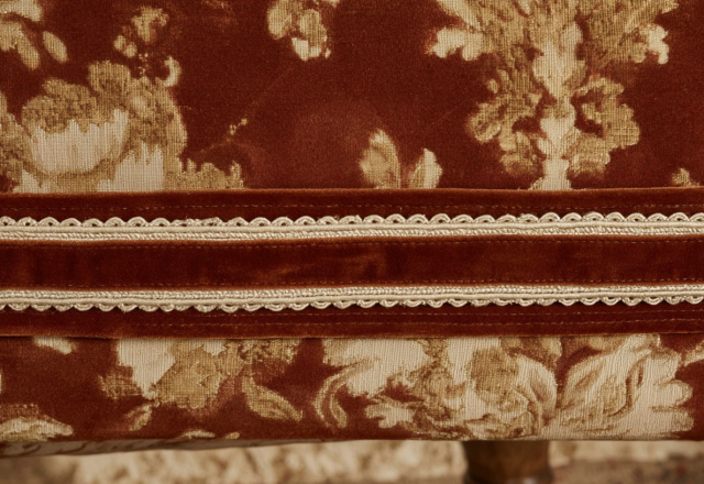 Close-up view of intricate upholstery trim details featuring crimson fabric and gold braided gimp.