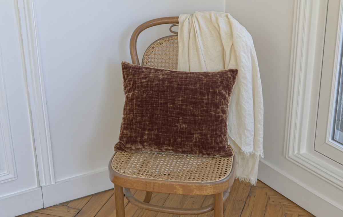 Vintage cane back chair styled with a velvet pillow and cream throw blanket in a corner with herringbone floors.