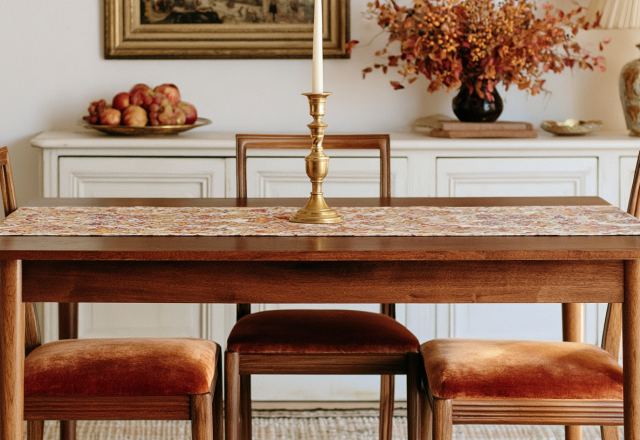 A midcentury dining table styled with velvet chairs, a brass candlestick, and a seasonal table runner.