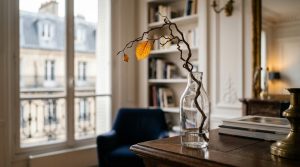 Minimalist home styling featuring a curved natural branch in a glass vase on a wooden desk near a tall window.