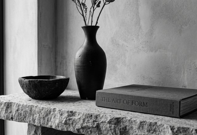 Minimalist shelf styling featuring a dark ceramic vase, stone bowl, and neutral book on a stone ledge.