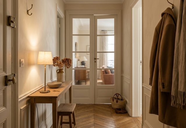 Narrow hallway decor featuring a shallow wooden console table, warm table lamp, and reeded glass French doors.