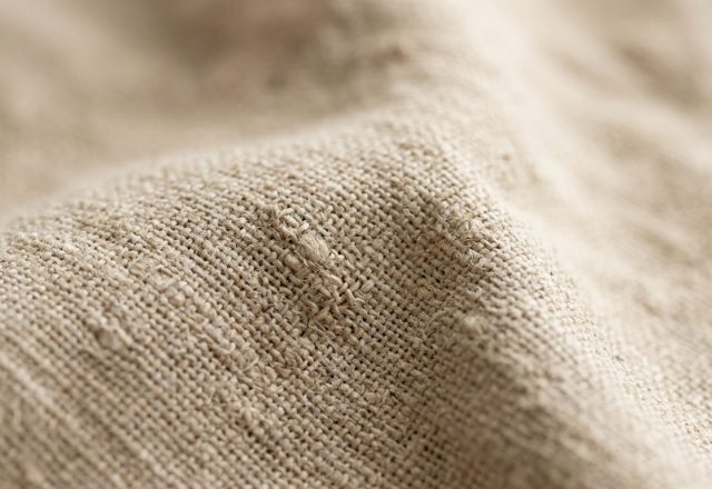 Close-up shot of natural linen fabric showing detailed weave texture and folds.