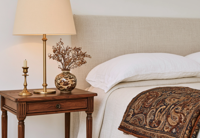Neutral bedroom styling featuring a vintage wooden nightstand, brass lamp, and textured bedding.