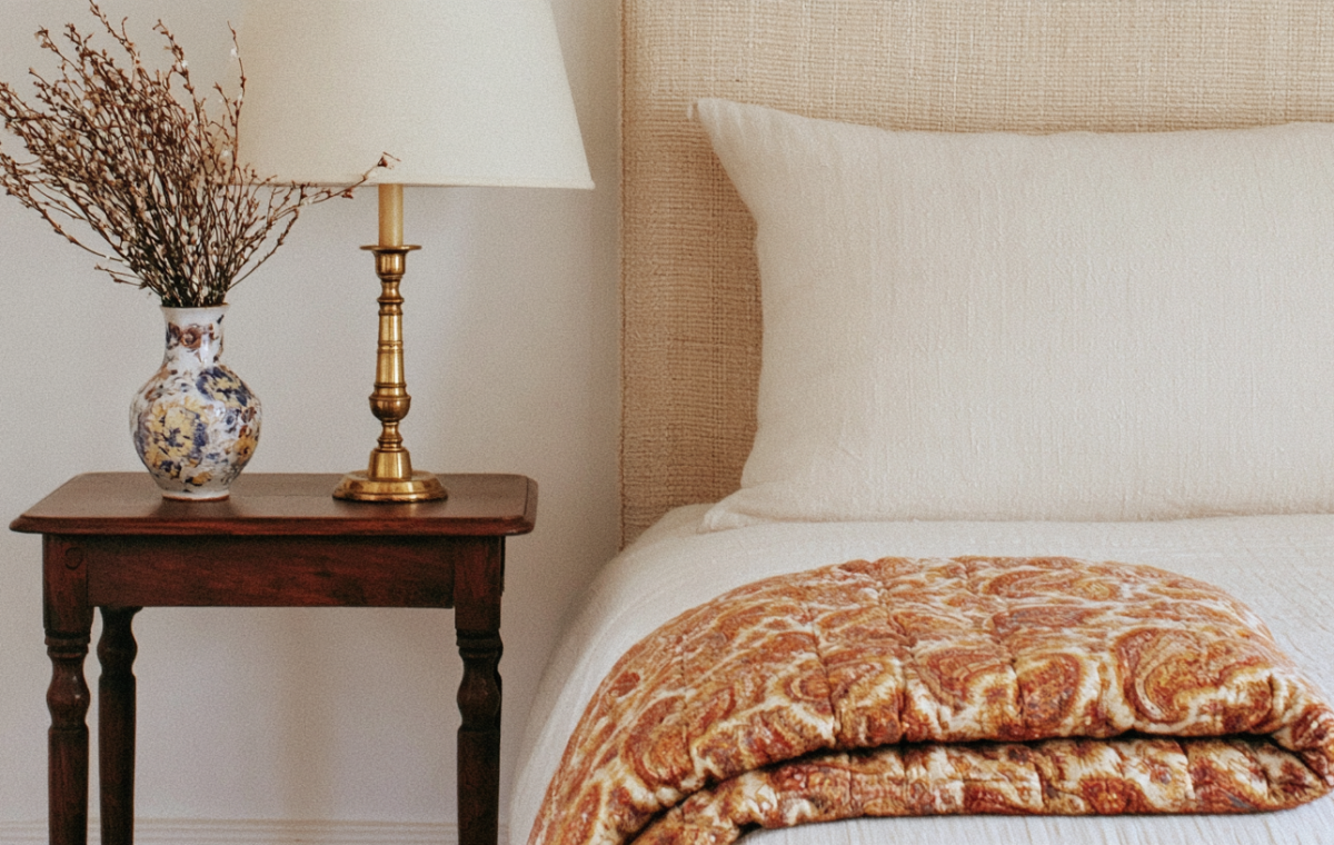 Neutral bedroom styling featuring textured bedding, a wooden nightstand, and a brass lamp.