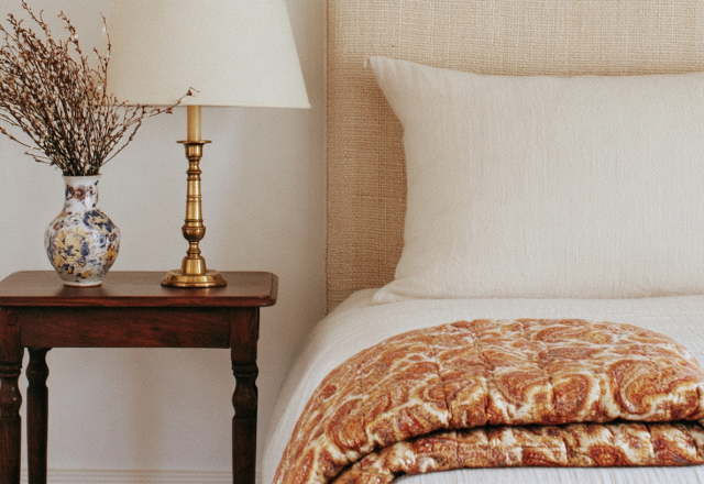 Neutral bedroom styling featuring textured bedding, a wooden nightstand, and a brass lamp.