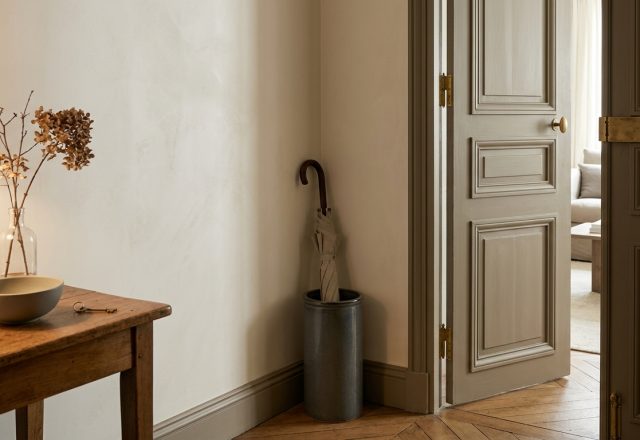 Neutral entryway decor featuring a wooden console table, beige walls, and a ceramic umbrella stand in a hallway.
