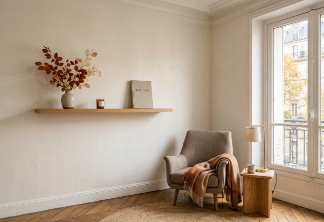 Minimalist neutral living room styling featuring a floating wooden shelf, armchair, and natural light