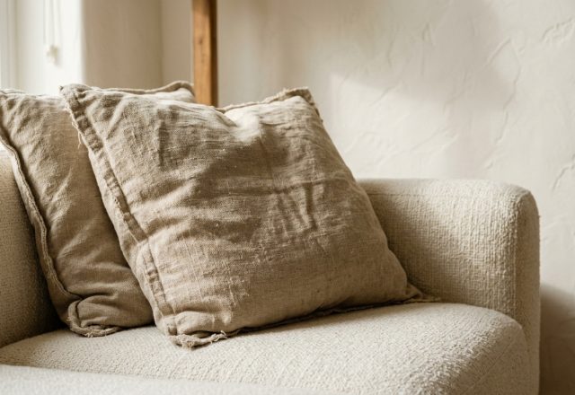 Neutral living room throw pillows in coarse linen resting on a textured cream sofa with warm white plaster walls.