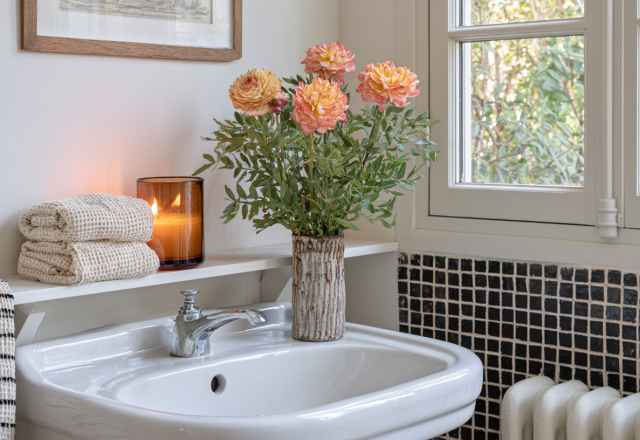 Charming powder room decor featuring fresh peach flowers in a ceramic vase, amber candle, and folded linen towels.