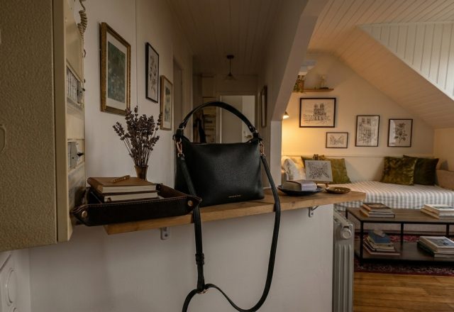 Stylish entryway drop zone featuring a black leather handbag on a wooden ledge with a catch-all tray and dried flowers.