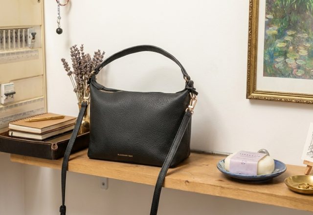A black leather handbag resting on a wooden entryway shelf with decor items.