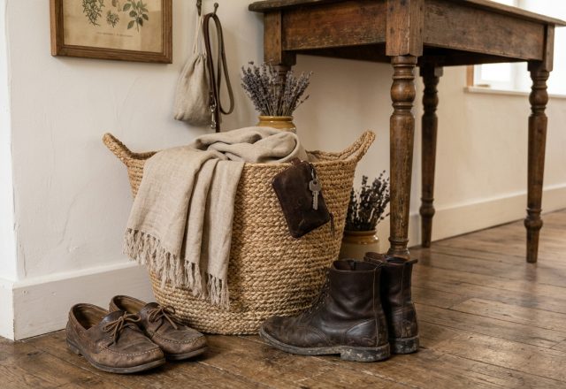 Rustic mudroom drop zone with woven basket, leather boots, and natural textiles on wooden floors.