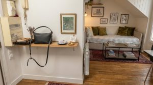 A clean small entryway drop zone featuring a floating wooden shelf and a black leather handbag.