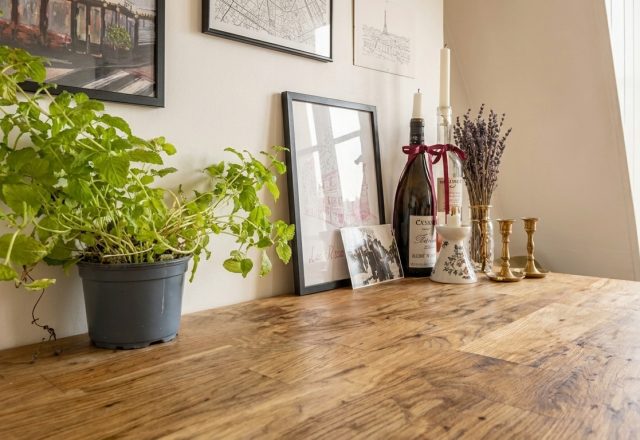 Wooden dining table decor styled with potted mint, framed art, and glass bottles in a bright room.