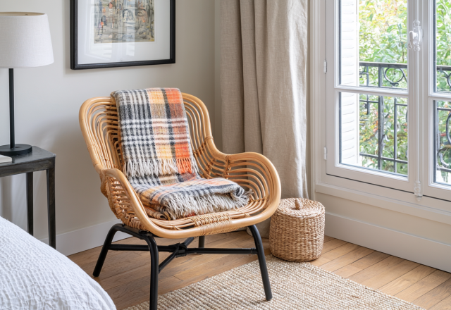 Cozy bedroom corner featuring a rattan armchair styled with a tartan throw blanket and a black side table.