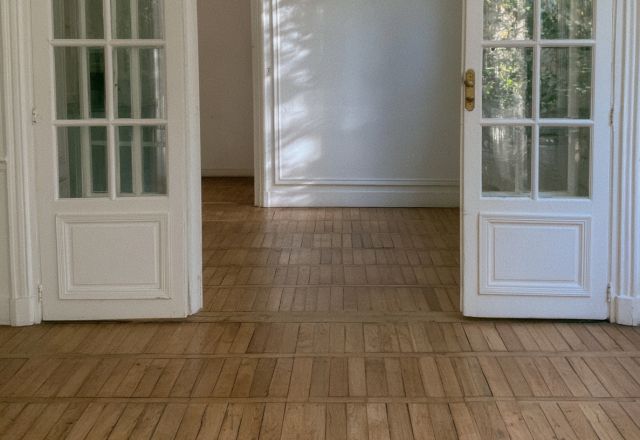 Parquetry wood floors inside a historic room with white double doors.