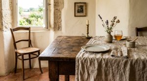 Rustic dining room decor featuring an antique wooden table, linen tablecloth, and a vintage chair by a sunny window.