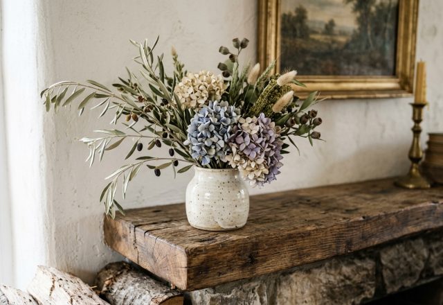 Rustic fireplace mantel decor styled with a ceramic vase, dried botanicals, vintage books, and a brass candlestick.