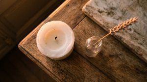 White pillar candle and dried botanical stem in a glass bottle on a rustic wooden table.