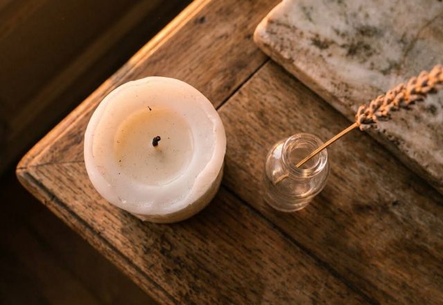 White pillar candle and dried botanical stem in a glass bottle on a rustic wooden table.