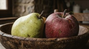 A rustic wooden bowl filled with a fresh pear and an apple on a kitchen counter.