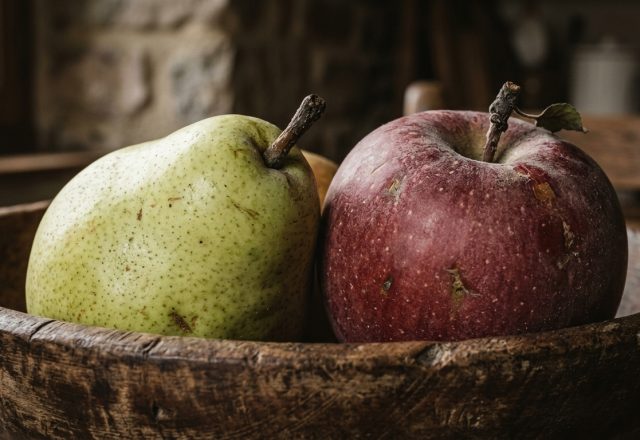 A rustic wooden bowl filled with a fresh pear and an apple on a kitchen counter.