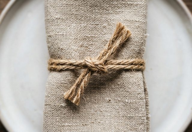 A rustic table setting featuring a neutral linen napkin tied with jute twine on a ceramic plate.