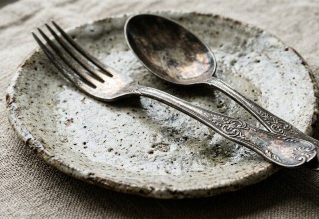 Rustic tableware featuring a handmade ceramic plate, vintage fork, and spoon on linen.