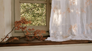 Rustic window sill decor featuring a foraged autumn branch and a sheer embroidered white curtain.