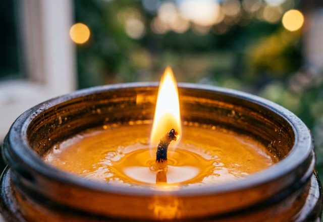 Close-up of a lit amber jar scented candle with a glowing flame and golden wax pool.