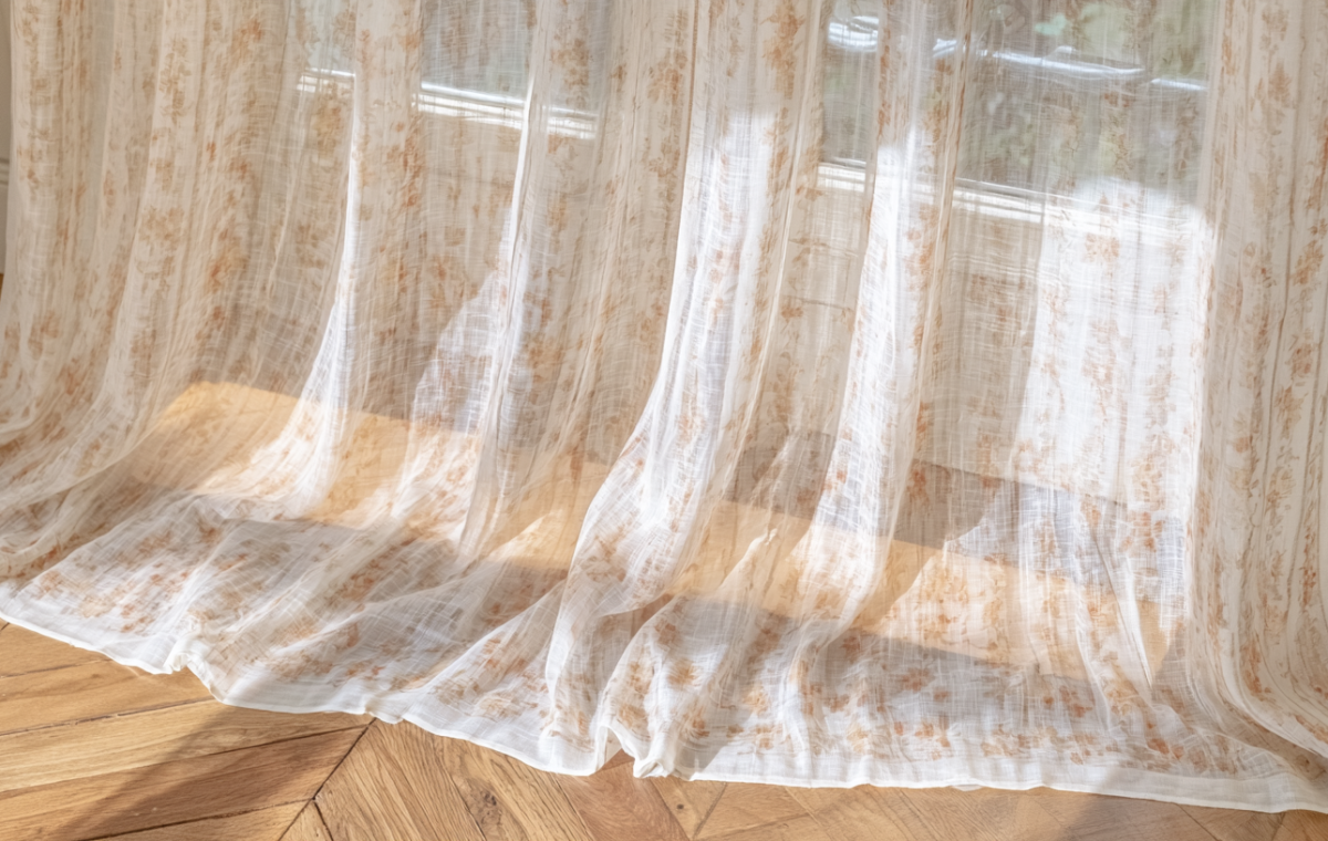 Sheer linen curtains with botanical prints pooling gracefully on herringbone hardwood floors.