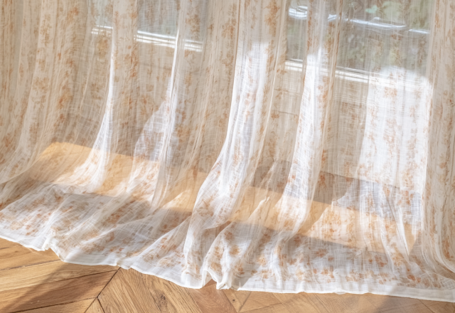 Sheer linen curtains with botanical prints pooling gracefully on herringbone hardwood floors.