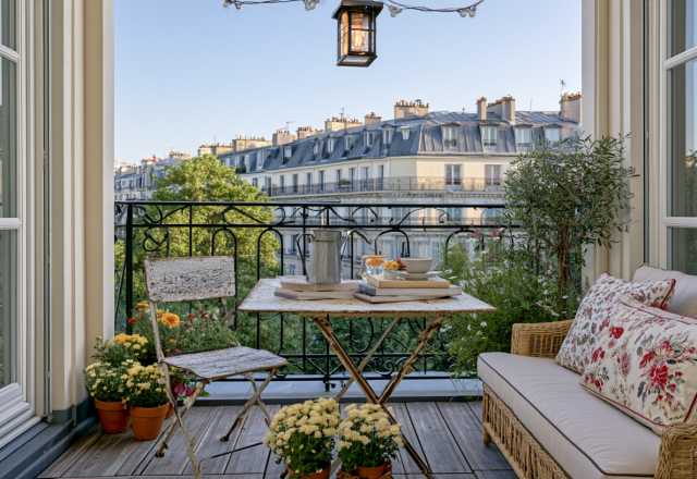 Charming small balcony design featuring a vintage bistro set, floral loveseat, and potted flowers overlooking city rooftops.